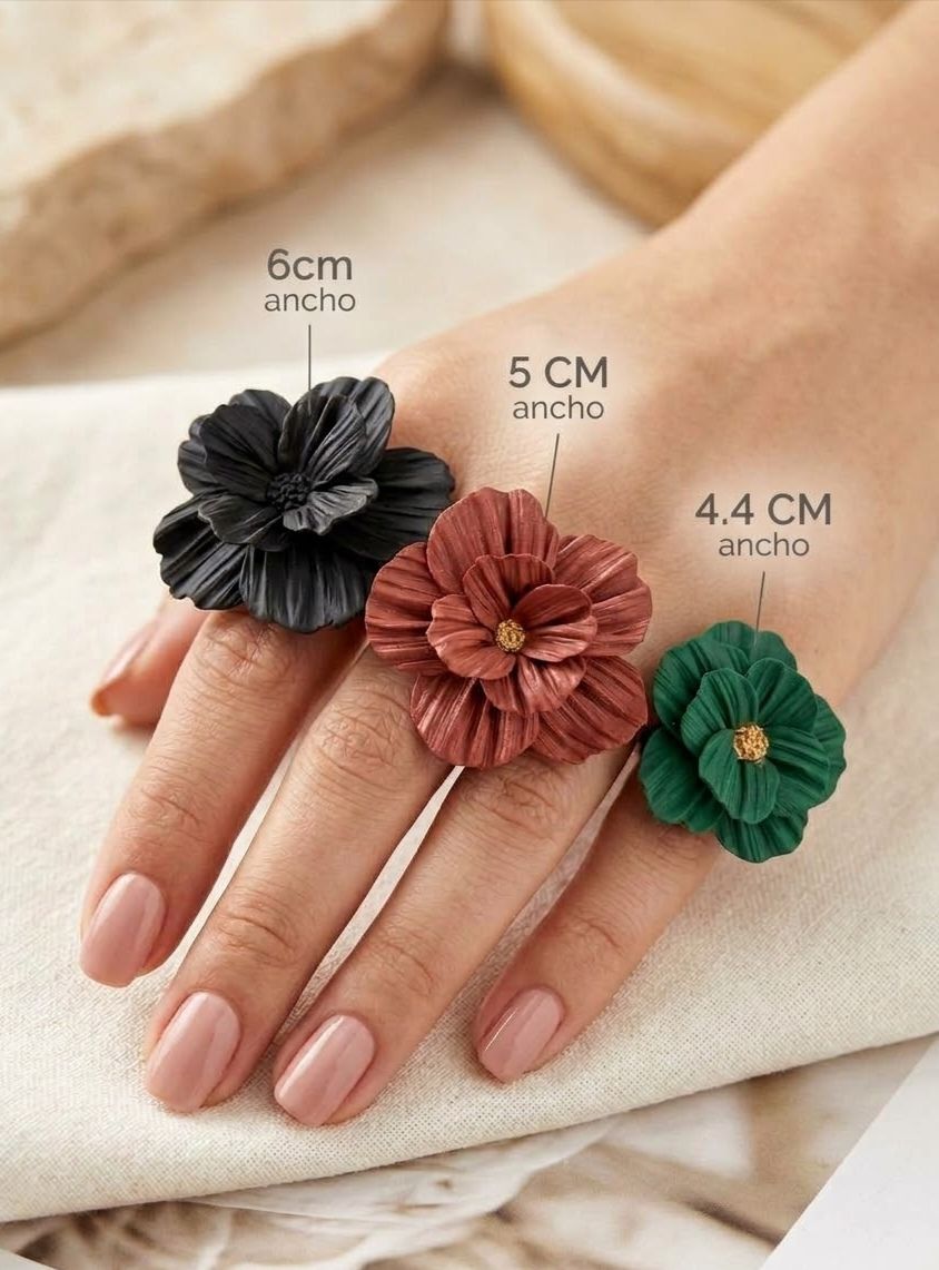 Tres anillos de flor de arcilla polimérica en una mano: negro de 6 cm, terracota de 5 cm y verde de 4,4 cm de ancho